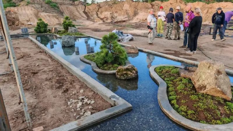Водное зеркало парка с каменным островом, вокруг — молодые сосны и насыпные холмы